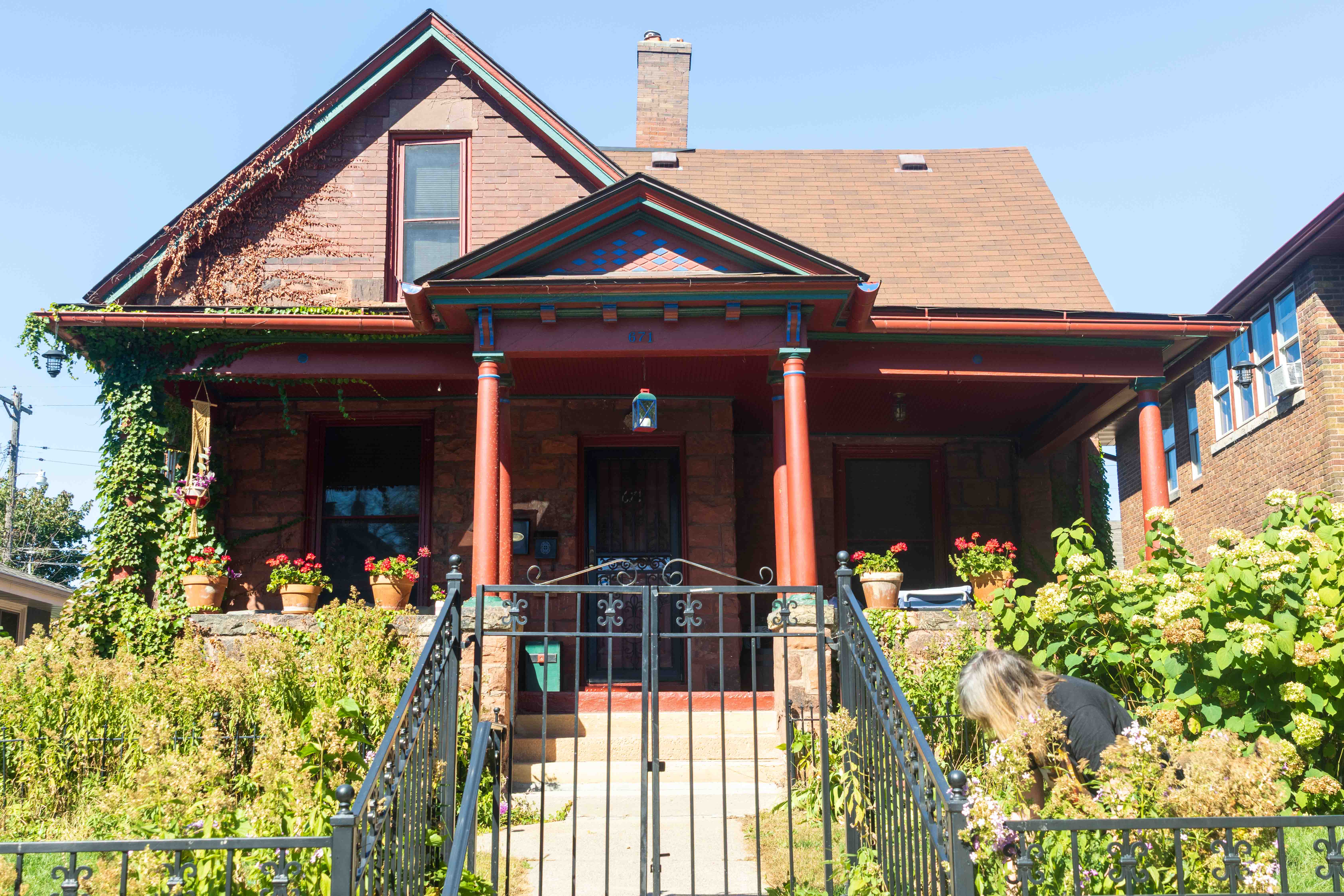 A wrought Iron fence and gardens in front of 671 Geranium Ave., a red stone and brick house.